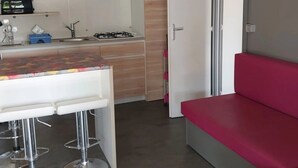 A modern kitchen with a dining area, a red bench, and a door leading to another room. - Camping 3 étoiles - Piscine (Arces)