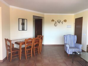 Uma sala de jantar com uma mesa e cadeiras de madeira, uma poltrona listrada em azul e detalhes decorativos nas paredes.
