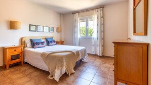 Een slaapkamer met een bed, nachtkastjes, een kledingkast en een raam met gordijnen.