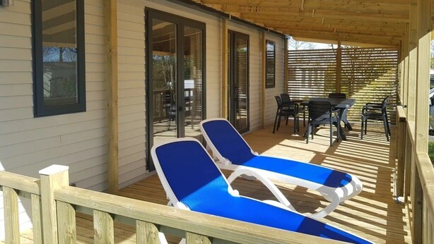 Een overdekt terras met twee loungesteilen, een tafel en stoelen.