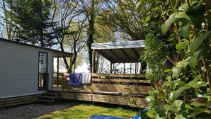 Een achtertuin met een houten terras, een overdekte zithoek en twee loungestoelen.