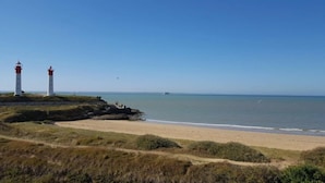 Een kustlandschap met twee vuurtorens, een zandstrand en een heldere lucht.