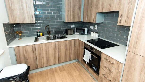 A modern kitchen with wooden cabinets, a black stove, a microwave, and a sink. - Nay Apartment Two-Bedroom Appt in Coventry (Longford)