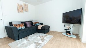 A living room with a sectional sofa, a flat-screen TV, and a light-colored rug. - Nay Apartment Two-Bedroom Appt in Coventry (Longford)