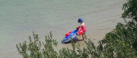 Escena de playa con un niño y un bote inflable azul.