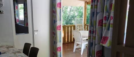 A room with a dining table, chairs, a sofa, a door, and a view of an outdoor deck.