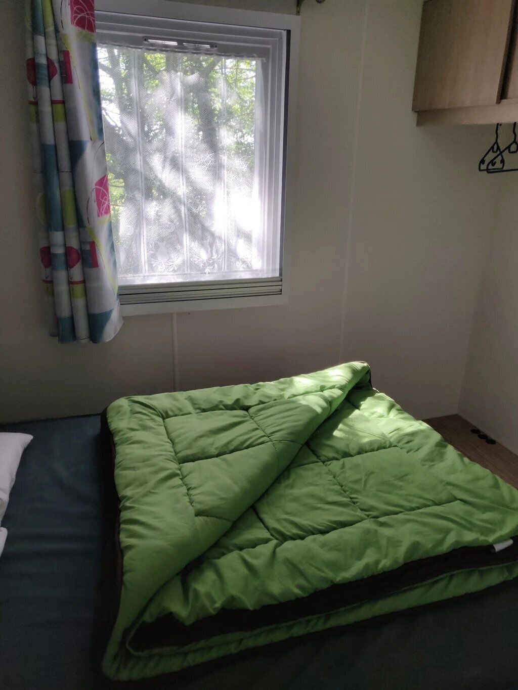 A small, single-bed room with a window, a curtain, and a green bedspread.