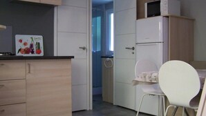 Eine kleine Küche mit Mikrowelle, Kühlschrank und einem Essbereich mit einem weißen Stuhl.