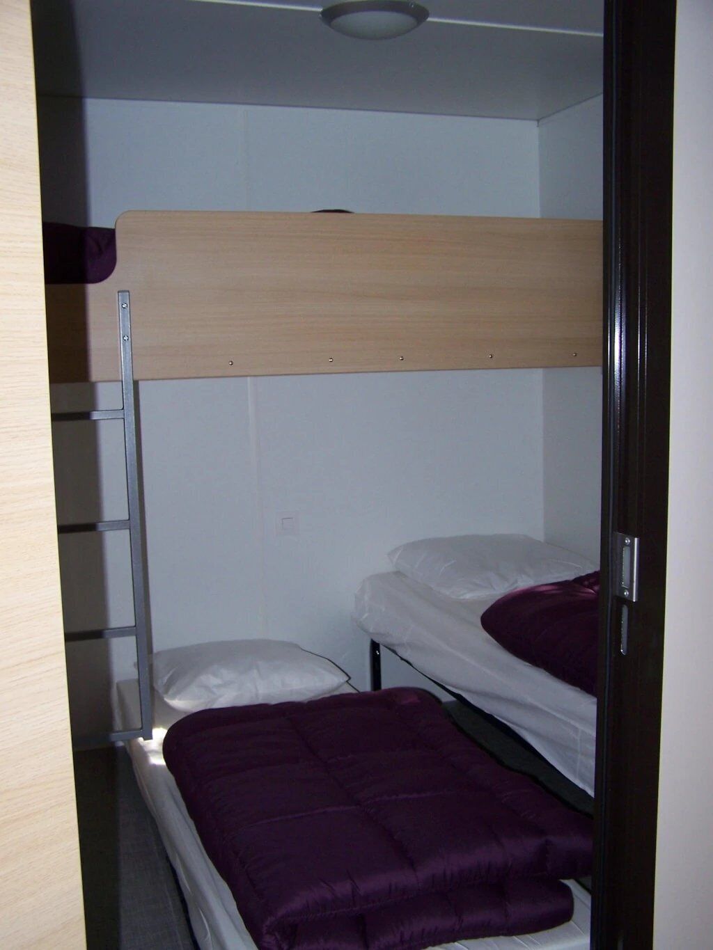 A bunk bed with a wooden top bunk and a lower bunk with a purple blanket.