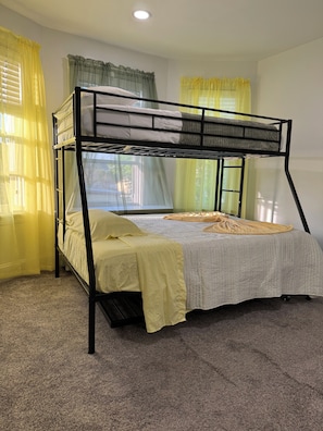 A bunk bed with a grey and white striped bedspread, yellow curtains, and a carpeted floor.