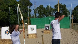 Dos personas practicando tiro con arco, con blancos y flechas sobre suelo arenoso.