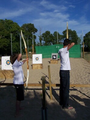 Two individuals practicing archery with targets and arrows on a sandy ground. - Camping 3 étoiles - Piscine  - ccbffee (Arces)