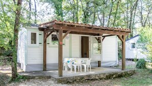 Una cabaña pequeña de un solo piso con un porche cubierto, una mesa con sillas y una ventana.