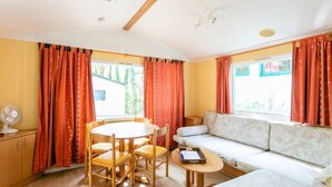 Une pièce comprenant une table à manger, des chaises, un canapé, une petite table avec un plateau et un ventilateur.