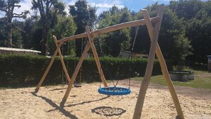 A swing set in a sandy area with trees in the background. - Camping 3 étoiles - Parc aquatique - ccbfgdh (Sainte-Eulalie-en-Born)