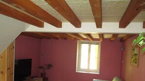 A small, cozy living space with a wooden ceiling, a television on a wooden stand, a sofa, and a window with curtains.