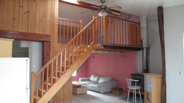 A multi-level room with a wooden staircase, a ceiling fan, a sofa, and a bar area.