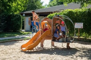 Ein Spielplatz mit Rutsche, Schaukeln und einem kleinen Gebäude im Hintergrund.