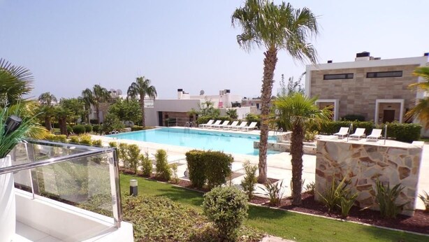 A swimming pool with lounge chairs, palm trees, and a modern building with stone facade. - Luxury 3 Bed 2 Bath Apt Near La Fuente Center, Beaches, Golf & Sun (VC)