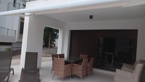 An outdoor patio with a table and chairs, a covered seating area, and a glass door leading to an interior space. - Luxury 3 Bed 2 Bath Apt Near La Fuente Center, Beaches, Golf & Sun (VC)