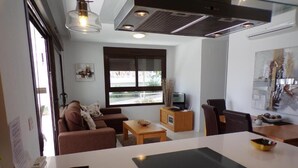 A modern kitchen with a central island, a dining area with a table and chairs, a sofa, and a large window. - Luxury 3 Bed 2 Bath Apt Near La Fuente Center, Beaches, Golf & Sun (VC)