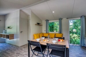 A dining area with a wooden table, black chairs, yellow cushions, and a view of greenery through the window. - Camping 3 étoiles - Piscine  - ccbfgef (Groléjac)