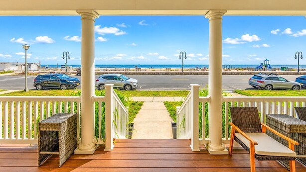 Un espacio al aire libre techado con vista a la playa, que incluye una terraza de madera, muebles de mimbre y una barandilla.