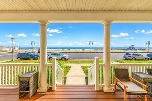 A covered outdoor area with a view of the beach, featuring a wooden deck, wicker furniture, and a railing. - Oceanfront Escape | 3BR/2BA w/ Views & Parking (Belmar)