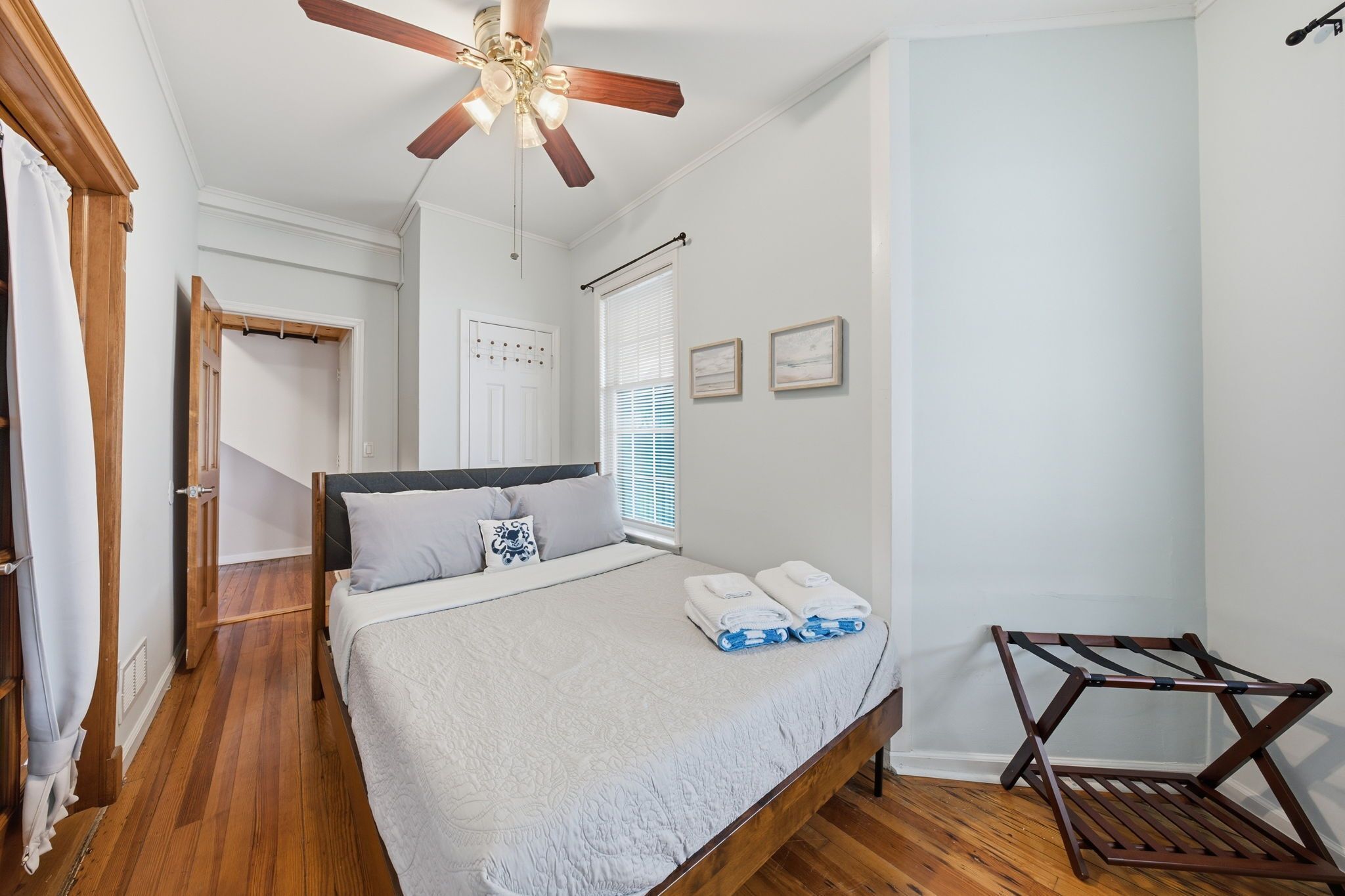 A bedroom with a bed, a ceiling fan, a window with blinds, and a wooden chair.