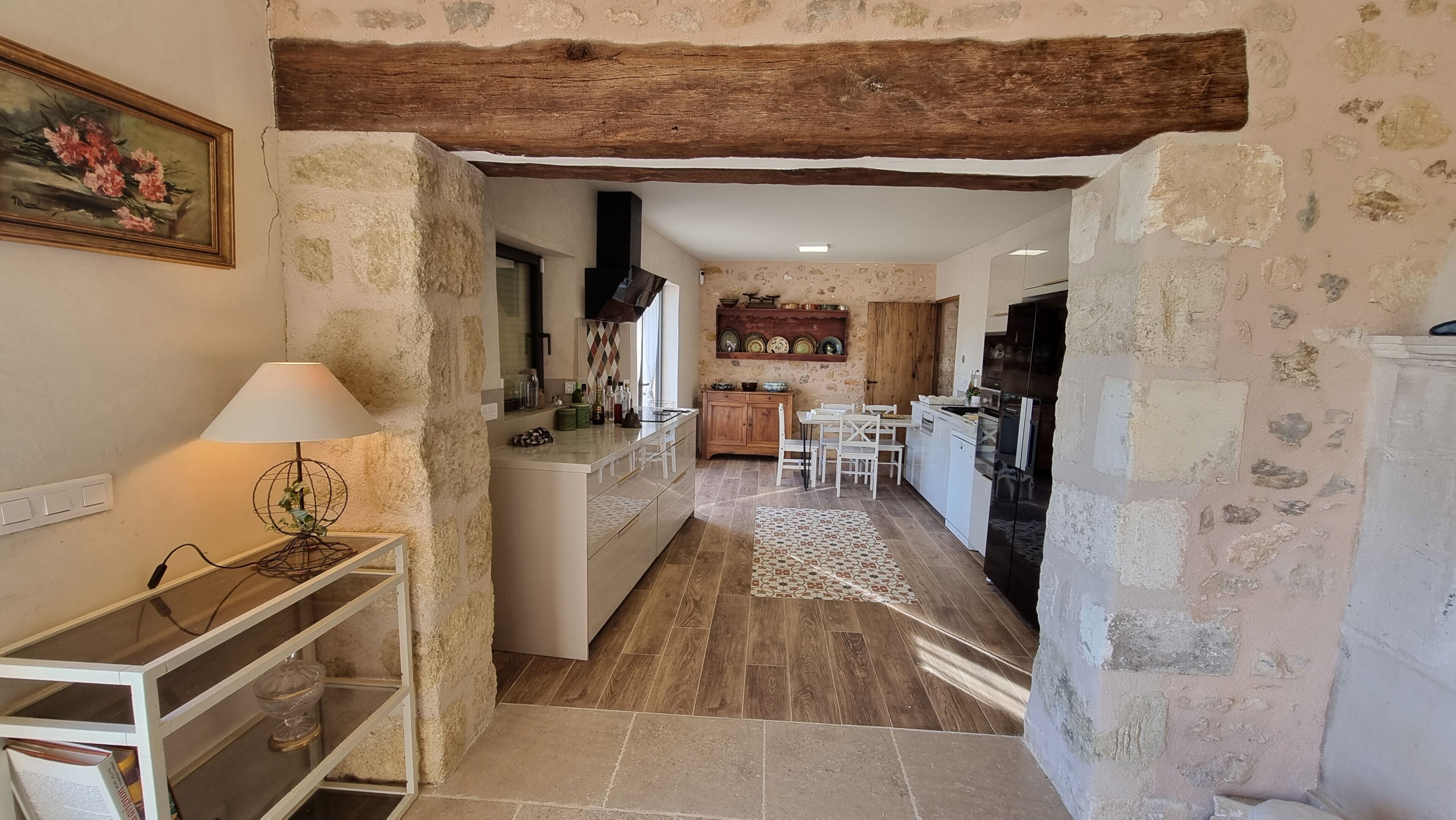 A narrow kitchen with a rustic stone wall, wooden beams, and a tiled floor.