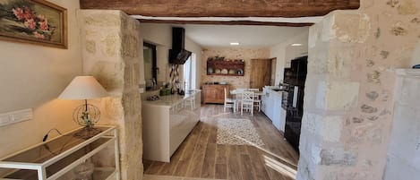 A narrow kitchen with a rustic stone wall, wooden beams, and a tiled floor.