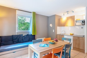 A compact living space with a sofa, dining table, chairs, a kitchen area, and a window with a curtain. - Accessible Cottage for 5 in Saumur (Saumur)
