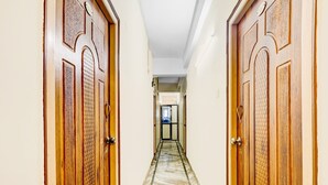 A hallway with wooden doors, a marble floor, and a view into another room. - Deluxe OYE Stays Visakhapatnam (Visakhapatnam)