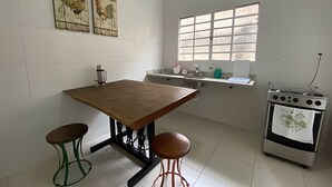 Cozinha com mesa de madeira, dois banquinhos, janela, fogão e obras de arte na parede.