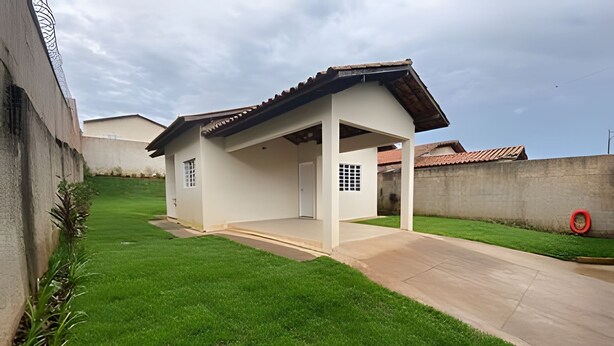 Uma casa térrea com varanda coberta, muro de concreto e gramado.