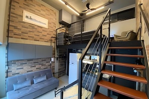 A modern living area with a sofa, a refrigerator, a staircase, and a ceiling fan.