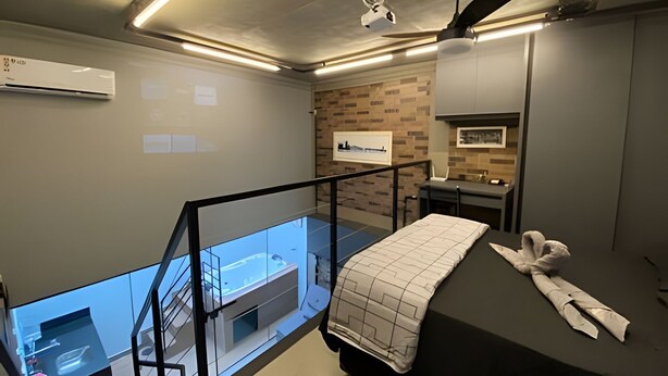 Quarto de hotel moderno com varanda, uma cama, uma escrivaninha e vista para a paisagem urbana.