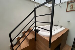 Une salle de bain moderne avec un meuble-lavabo en bois, une baignoire blanche et un escalier en métal noir.