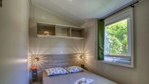 Ein Schlafzimmer mit einem Bett, einem Regal darüber, einem Fenster mit Vorhang und einer Wandleuchte.