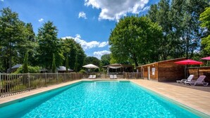 Ein rechteckiger Pool mit klarem, blauem Wasser, umgeben von einer Holzterrasse und einem Metallzaun.