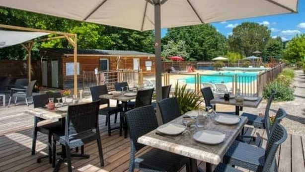 An outdoor patio with tables and chairs, a pool, and a wooden structure in the background. - Camping 3 étoiles - Piscine  - ccbfgfb (Groléjac)