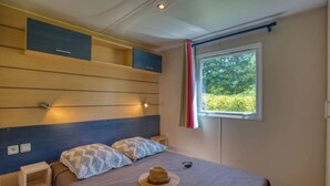 A bedroom with a bed, bedside tables, a window with curtains, and built-in storage cabinets. - Camping 3 étoiles - Piscine  - ccbfgfb (Groléjac)