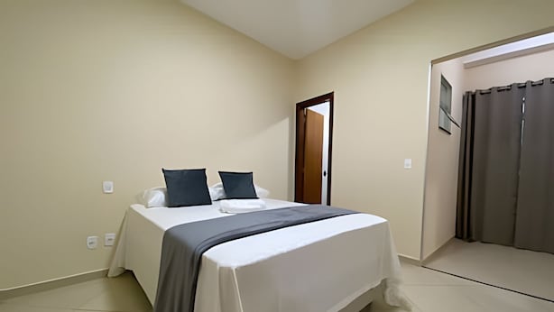 A bedroom with a bed, pillows, a table, a door, and a curtain.