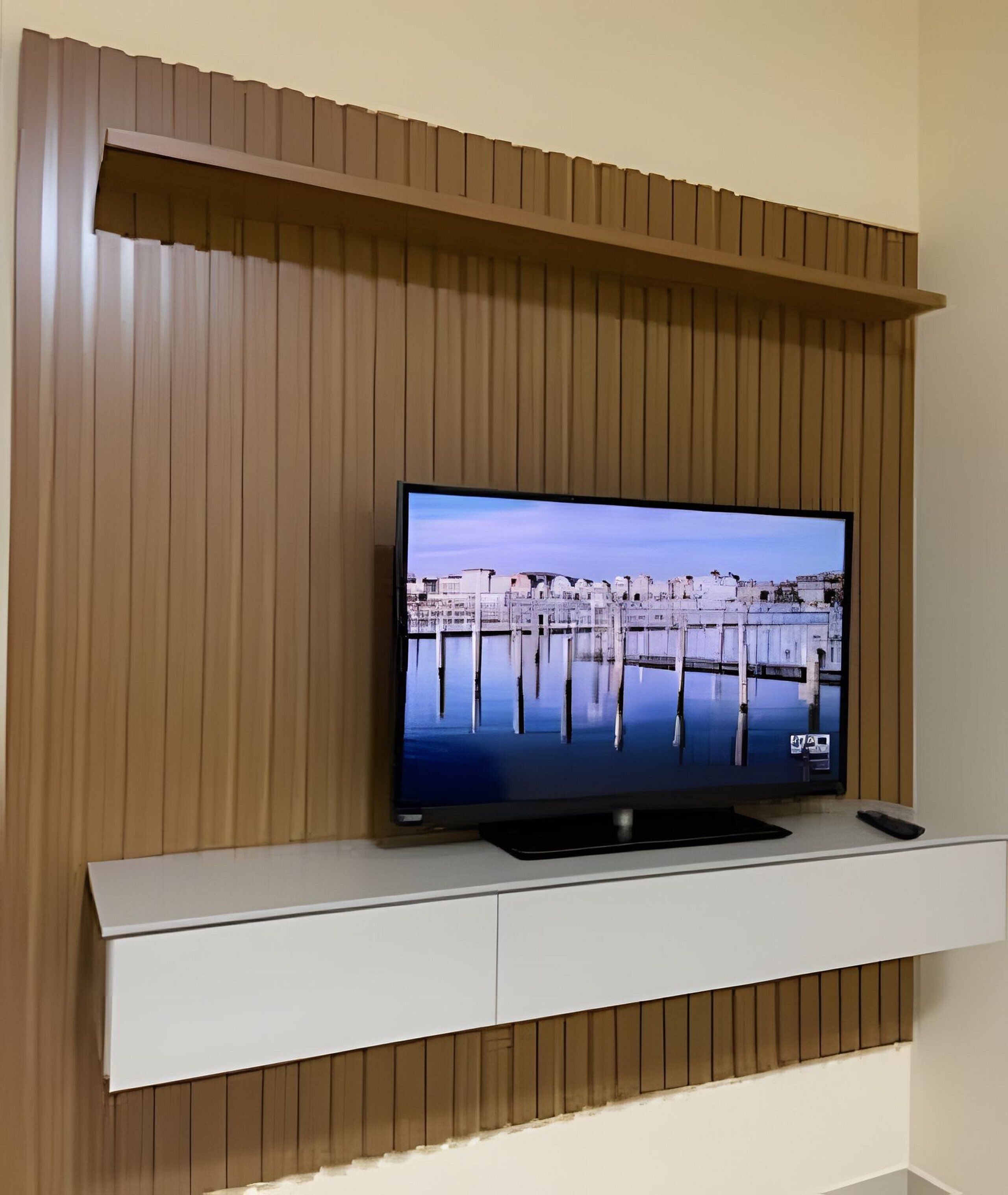 A flat-screen TV mounted on a wooden wall with a white entertainment unit below.