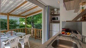 Un espace extérieur abrité, aménagé pour les repas, avec une table et des chaises, une cuisine équipée d’un évier, d’une cuisinière et d’un réfrigérateur.