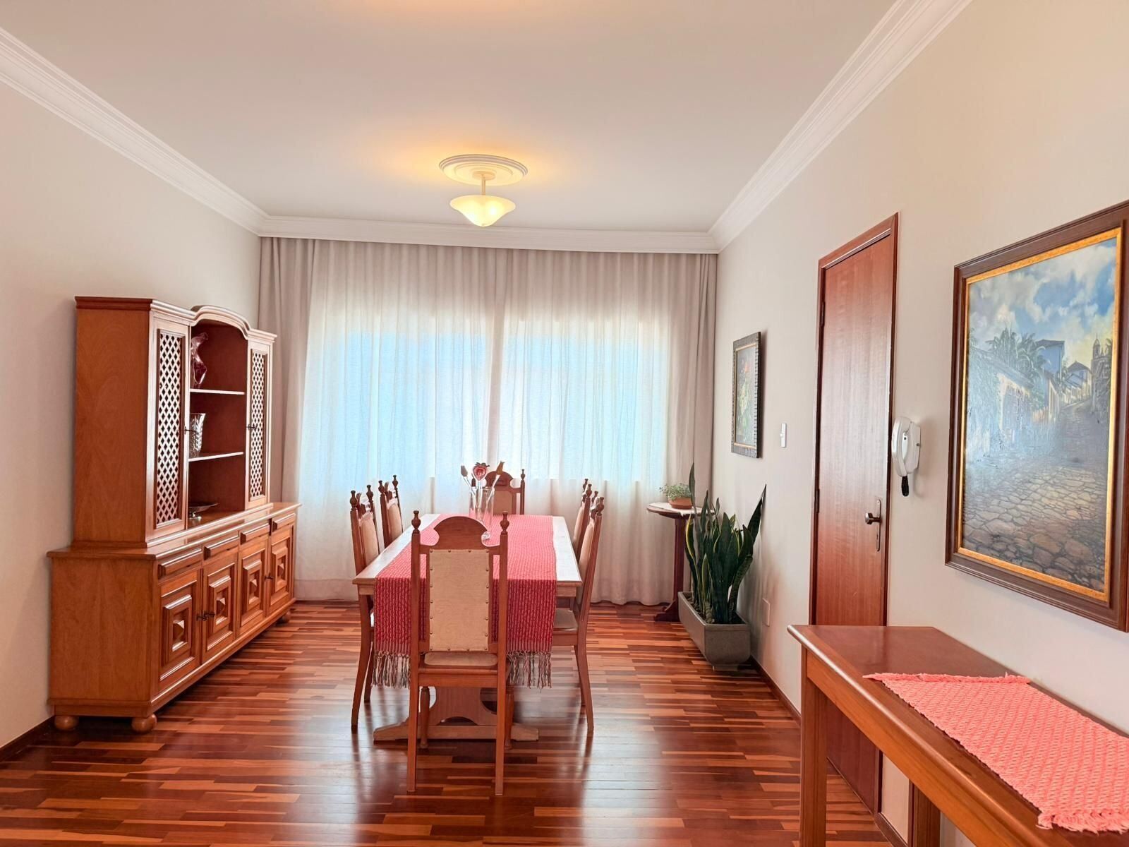 Una habitación con una mesa de comedor, sillas, un armario, una planta en maceta, un cuadro y una puerta.