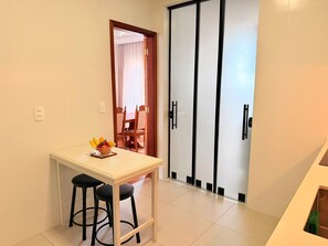 A room with a white table, two black stools, a fruit bowl, and a sliding door with black handles.