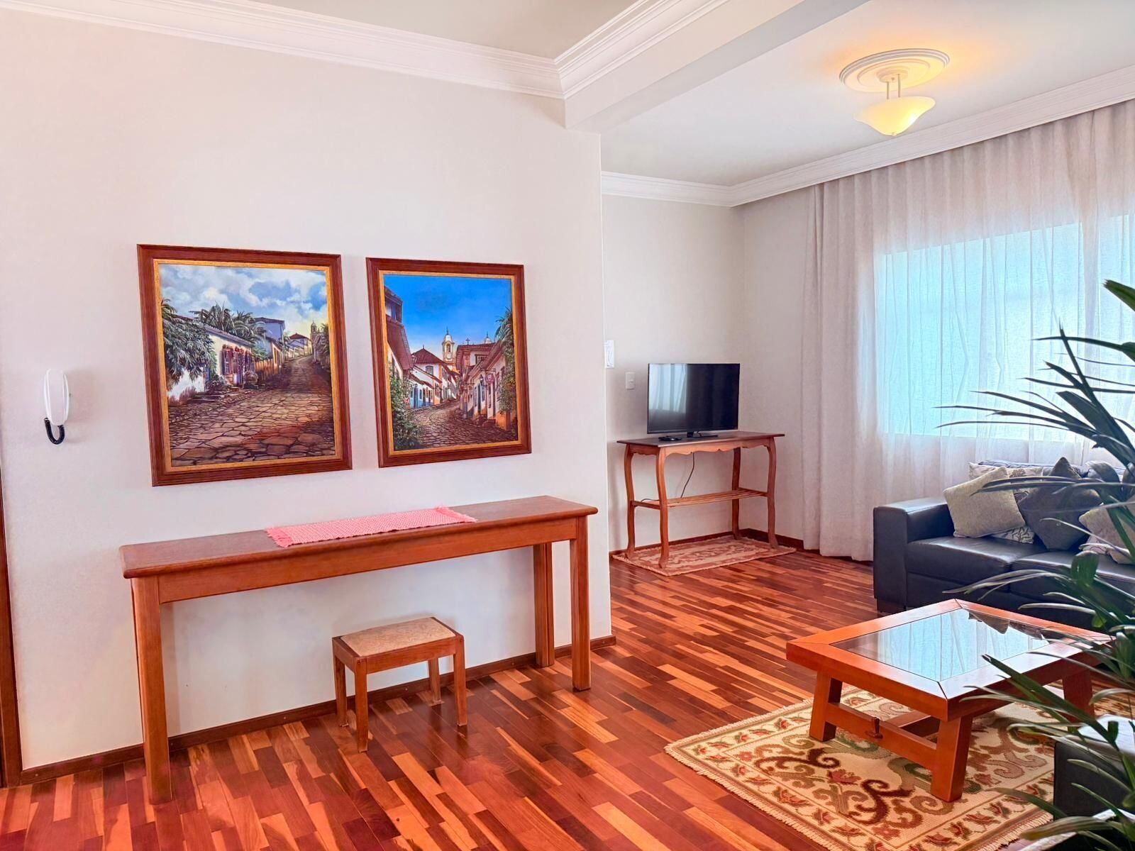A living room with a TV, wooden furniture, and two paintings on the wall.