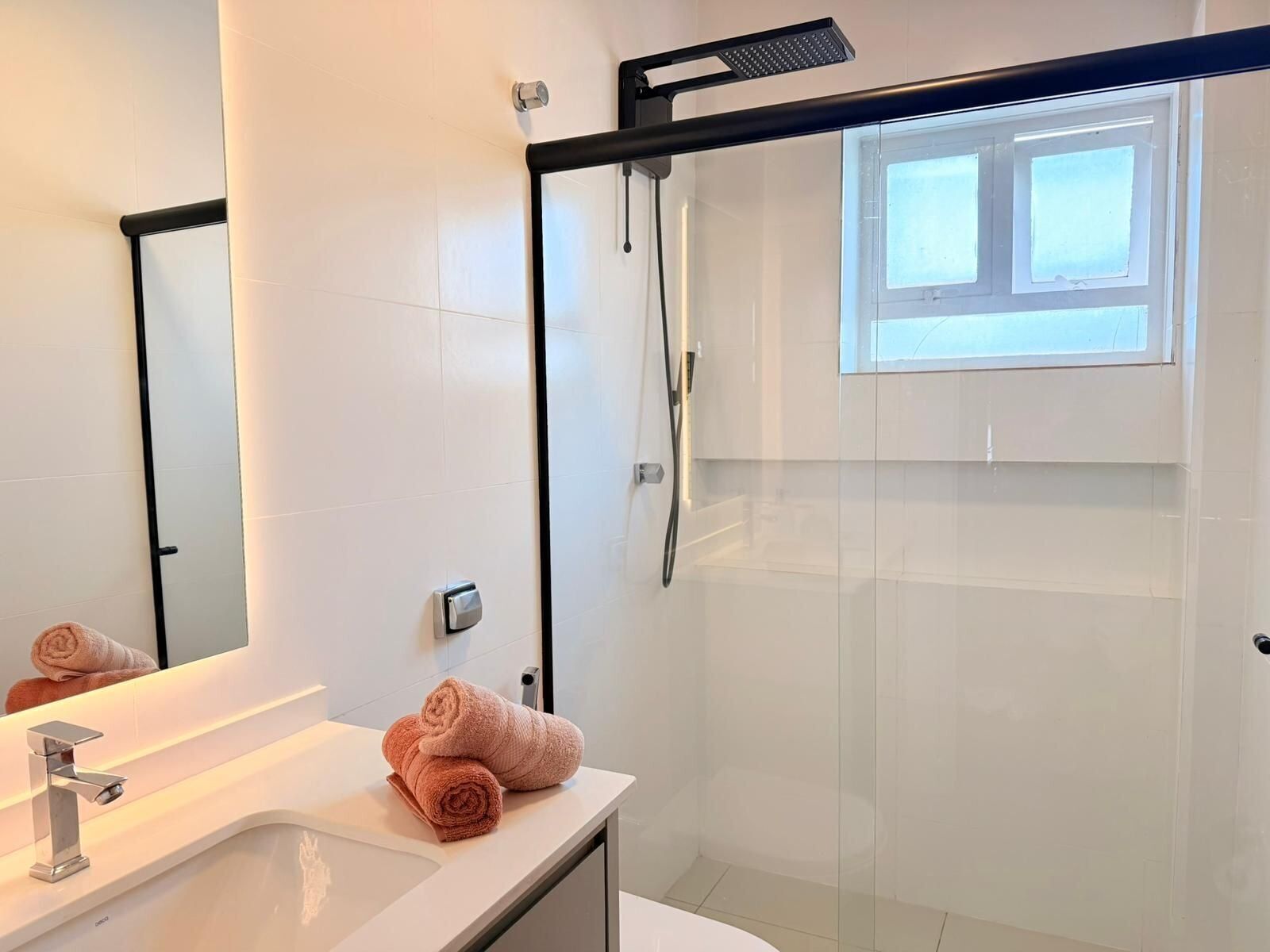 A modern bathroom with a glass shower enclosure, a large mirror, and a sink with a towel.