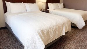 A hotel room with two beds, a nightstand with a lamp, and a carpeted floor. - Pecos Inn (Pecos)